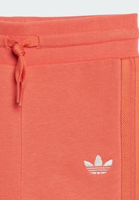 Korallenfarbene Sweatpants verfügen über einen strukturierten Stoff, einen elastischen Bund mit Kordelzug und ein weißes, gesticktes Logo auf der Vorderseite.