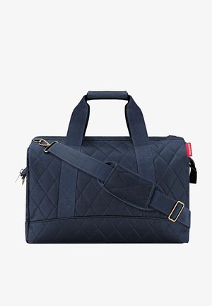 Sac en tissu matelassé bleu marine avec doubles poignées, bandoulière réglable, fermeture éclair et accents en métal doré.