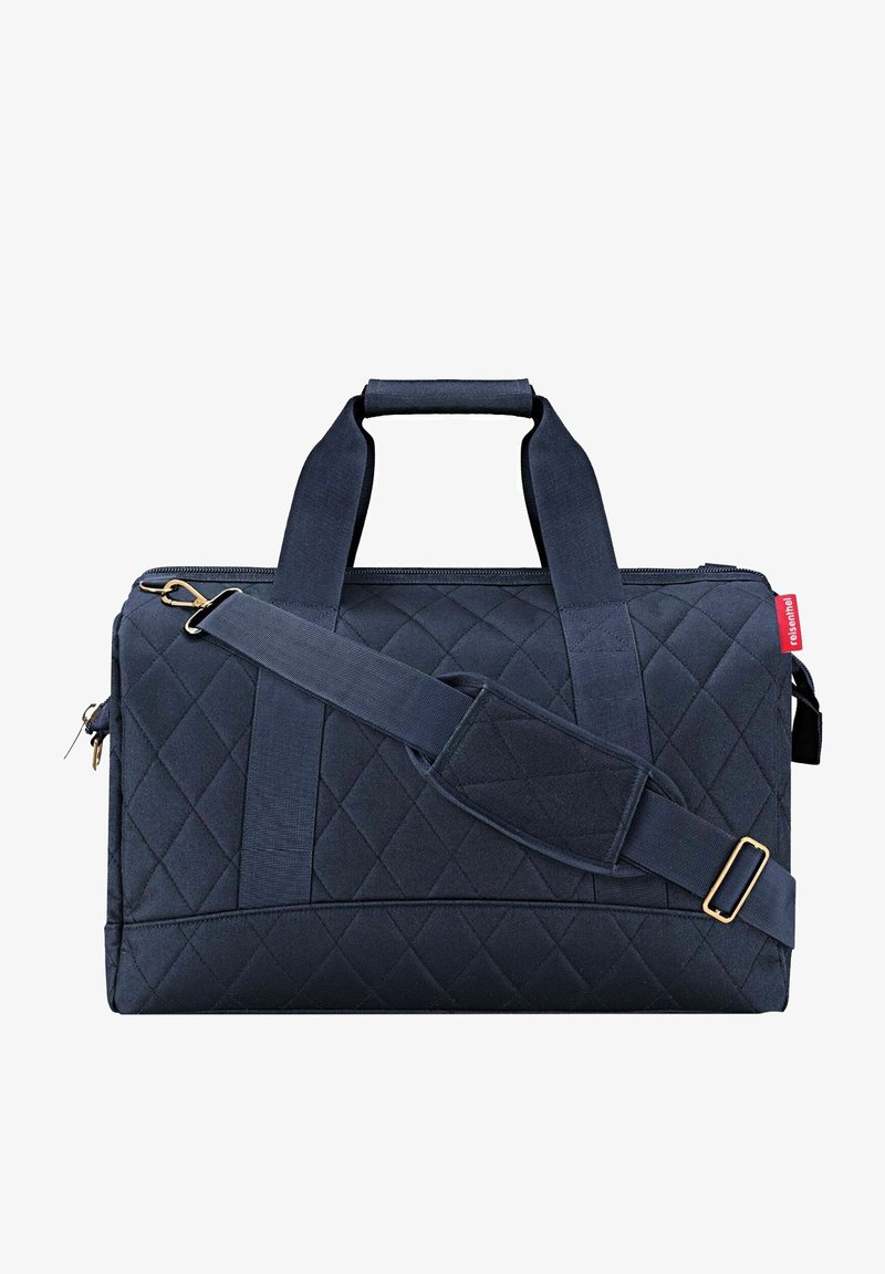 Dark blue quilted fabric duffle bag with dual top handles, adjustable shoulder strap, and gold-tone hardware for secure fastening.