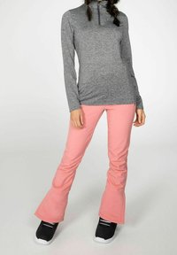 Top a maniche lunghe con collo alto e zip di colore grigio, abbinato a pantaloni rosa svasati. Calzature nere con suole bianche, tessuto di superficie liscio.