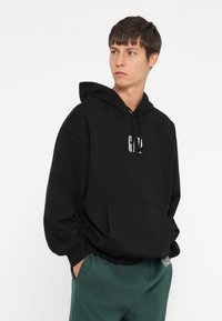 Black hoodie featuring a front pocket and drawstring hood, made from soft material with the "GAP" logo printed in white.
