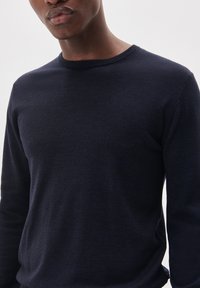 Granatowy sweter z dzianiny z długimi rękawami, okrągłym dekoltem i miękką fakturą. Minimalistyczny design bez widocznych wzorów ani elementów ozdobnych.