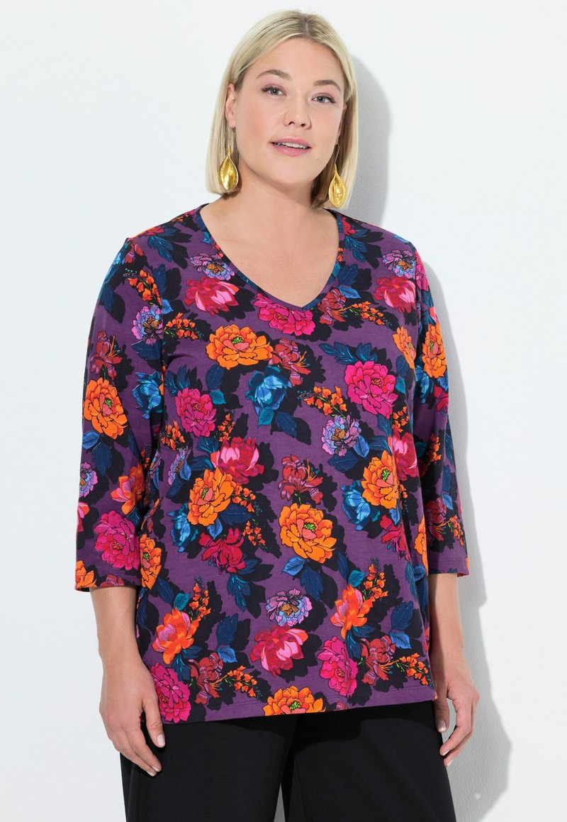 Lila Bluse mit drei Viertelärmeln. Verziert mit lebhaften orange, pink und blauen Blumen auf dunklem Hintergrund. V-Ausschnitt-Design.