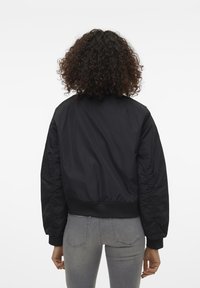 Czarna kurtka bomber o gładkiej fakturze, z prążkowanymi mankietami i dołem oraz lekko marszczonymi rękawami. Połączona z szarymi dżinsami.