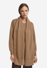 Jasnobrązowy, luźny sweter z długimi rękawami, dekoltem w serek i ozdobnymi dziurami w tkaninie, z prążkowanym wykończeniem u dołu oraz pasującym szalikiem.