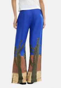 Niebieskie lniane spodnie szerokie w nogawkach z nadrukiem krajobrazu pustyni z kaktusami na dole. Lekki, przewiewny materiał o luźnym kroju.