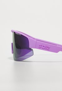 Lunettes de sport violettes avec un design arrondi, lentilles à dégradé foncé et branches texturées arborant la marque "bliz" embossée sur le côté.