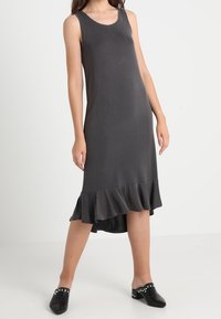 Sukienka bez rękawów w kolorze szarym z okrągłym dekoltem, z falbaniastym dołem i asymetrycznym krojem. Miękka tkanina o gładkiej fakturze.