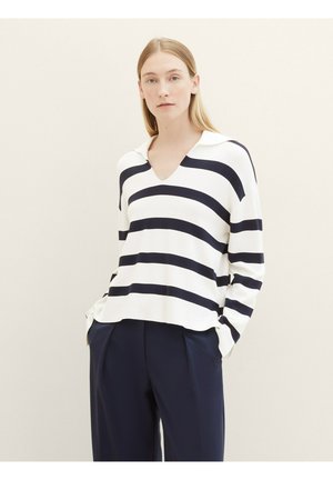 Pull blanc à rayures horizontales marines, décolleté en V, manches longues et fentes latérales. Associé à un pantalon droit marine. Texture lisse.