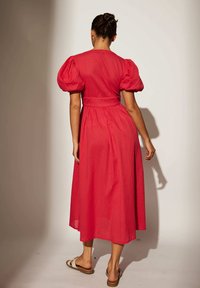 Röd midi-klänning i strukturerad tyg, puffärmar och knytning i midjan. Har en svängig kjol och en slät yta.