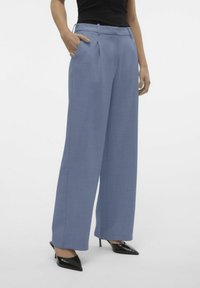 Lichtblauwe wijde broek met plooien, voorzien van zijzakken en een gladde textuur, gecombineerd met zwarte puntige hakken.