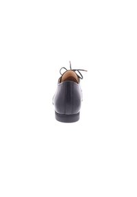 Chaussure en cuir noir avec orteil arrondi, petit talon et lacets fins noués à l'arrière. Texture lisse avec des détails de couture subtils.