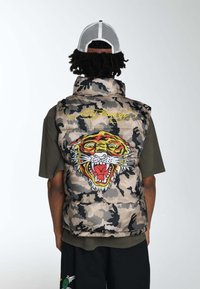 Kamerowy bezrękawnik z dużym haftowanym wzorem tygrysa i żółtym napisem "Ed Hardy" na plecach. Miękka tekstura, wypełniony dla ocieplenia.