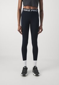 Granatowe legginsy kompresyjne z szerokim czarnym pasem, na którym znajduje się napis "NIKE PRO" w białym kolorze. Zaprojektowane dla idealnego dopasowania, odpowiednie do aktywności sportowych.