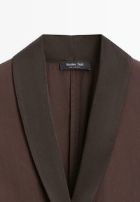 Donkerbruine blazerkraag met brede revers en een zwart label "Massimo Dutti Made in Morocco" aan de binnenkant vastgenaaid.