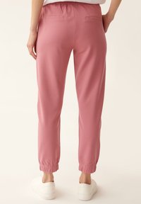 Pink sweatpants with a relaxed fit, elastic waistband, and gathered cuffs. Features two small back pockets. Soft cotton blend material.