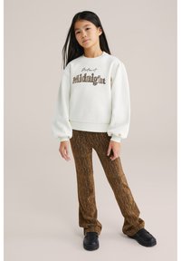 Balta džemperis su žodžiu "Midnight" tamsiai ruda spalva, pūstomis rankovėmis, derinamas su rudos spalvos raštuotomis platėjančiomis kelnėmis ir juodais masyviais batais.