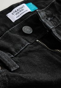 Jeans din denim negru cu un design de înălțime medie, dotate cu un buton metalic, închidere cu fermoar și o etichetă care spune "S. Straight, Fabricat în Pakistan."