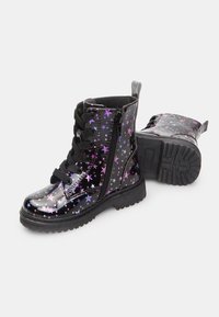Botas de tobillo de charol negro con estampado de estrellas moradas y rosas, cordones negros, cremallera lateral y suela de goma texturizada.