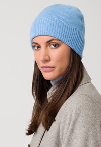 Bonnet en tricot bleu clair avec une texture côtelée, légèrement surdimensionné, associé à un manteau gris et un col roulé, montrant un gros plan du chapeau.