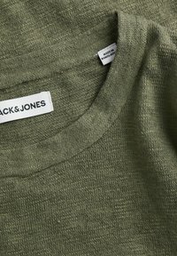 Pull vert en laine montrant l'encolure avec l'étiquette de la marque "JACK & JONES" et une petite étiquette indiquant "Made in Bangladesh."