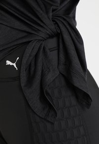 Černé sportovní legíny s texturovanými detaily a decentním logem. Tkanina má hladký povrch, doplněná o zkroucení v černém tričku.