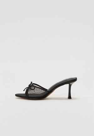 Sort hællet mule med netoverdel, tynde stropper og en dekorativ knude. Har en slank, spids hæl og en struktureret indersål.