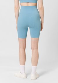 Modré žebrované šortky s vysokým pasem sahající do poloviny stehna, v kombinaci s bílými teniskami a kotníkovými ponožkami. Hladká textura, přiléhavý střih.