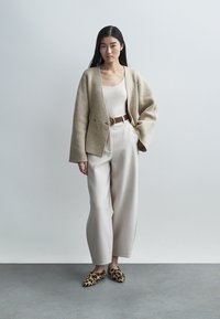 Μπεζ μάλλινο σακάκι πάνω από λευκό τοπ, σε συνδυασμό με ανοιχτό γκρι παντελόνι φαρδιάς γραμμής. Διακοσμημένο με καφέ ζώνη και mule με λεοπάρ σχέδιο.