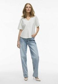 Hellgraues, kurzärmliges V-Ausschnitt-Oberteil kombiniert mit hellblauen, locker sitzenden Jeans und beigen High Heels. Einfaches, klares Design.