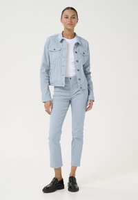 Veste en jean bleu clair avec poches avant, associée à un jean slim bleu clair assorti. Des mocassins noirs ajoutent du contraste à la tenue.
