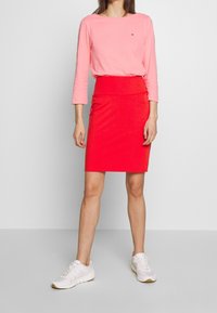 Rosa Langarmshirt kombiniert mit einem roten Bleistiftrock. Das Outfit zeichnet sich durch eine enganliegende Passform und glattes Material aus. Getragen mit weißen Sneakers.