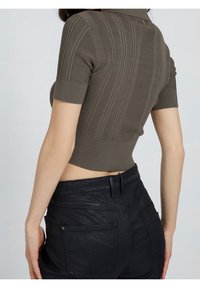 Top court à manches courtes en tricot vert olive avec des nervures verticales. Associé à un pantalon noir taille haute avec des poches arrière.