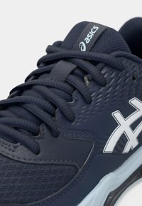 Marineblå atletiske sko med teksturert mesh-overdel, flate lisser og hvit logoaksent. Har polstret krage og sømløs konstruksjon for komfort.