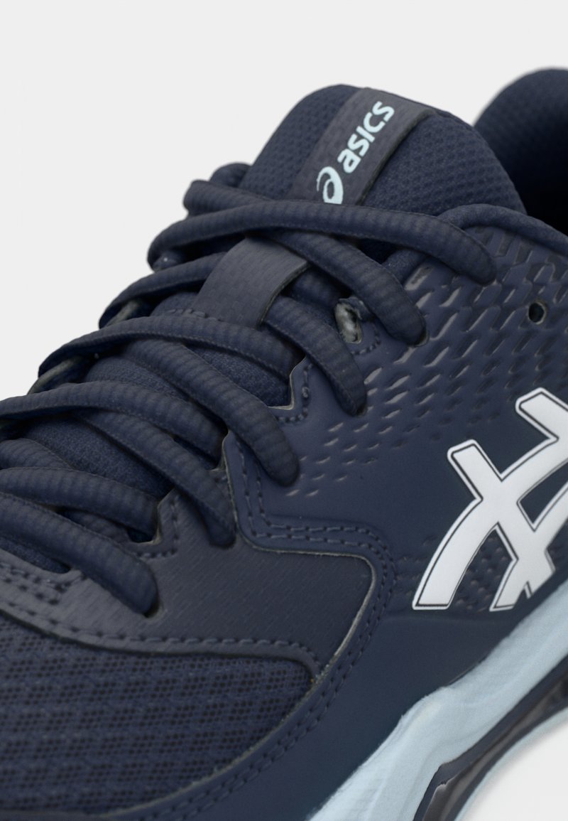 Chaussures de sport bleu marine avec tige en maille texturée, lacets plats et logo blanc en accent. Dotées d'un col rembourré et d'une construction sans coutures pour le confort.