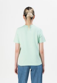 Mintgrønn bomull T-skjorte med korte ermer og rund hals, vist fra baksiden. Kombinert med blå denim jeans.