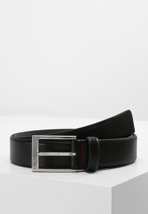 Ceinture en cuir noir avec une texture lisse, boucle rectangulaire en argent et un détail de couture rouge le long du bord. Design plat, esthétique moderne.