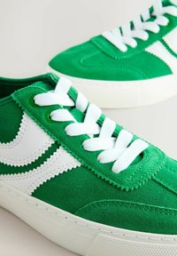 Žalios zomšinės sportbačiai su baltais odiniais akcentais, balti raišteliai, tekstūruota paviršiaus struktūra ir guminis padas. Dviejų tonų dizainas su siuvinėjimo detalėmis.