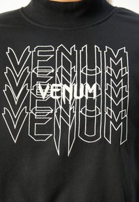 Sweatshirt noir à col montant avec le texte géométrique "VENUM" en blanc, en différentes tailles et orientations ; texture de tissu douce.