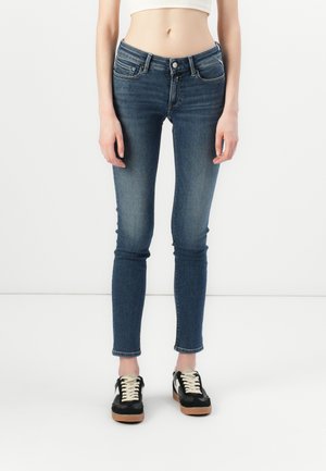 Mørkeblå denim skinny jeans med mid-rise liv, fem-lommestil og let falmning. Kombinert med sorte og hvite sneakers.