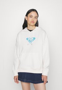 Light beige hoodie made of soft fabric, featuring a turquoise geometric logo on the chest and a front pocket. Loose fit with drawstring hood.