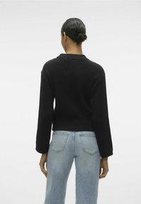 Maglione nero a coste con scollo ampio e design cropped, abbinato a jeans chiari a vita alta con taglio classico e tasche.