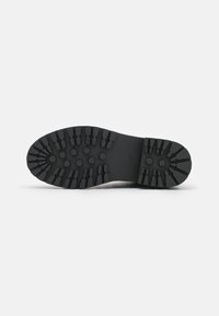 Suela de zapato de goma negra con profundos surcos hexagonales y lineales, con el tamaño número 37 grabado cerca del centro sobre un fondo blanco liso.