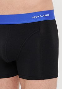 Schwarze Baumwoll-Boxershorts mit einem blauen Elastikbund, der den Text "JACK & JONES" in Weiß aufweist. Beinhaltet eine enge Passform und gestickte Details.