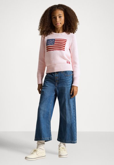 Lys rosa strikket genser med et amerikansk flaggdesign i rødt og blått. Kombinert med vide blå denimjeans og hvite joggesko.