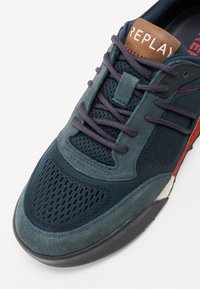 Baskets bleues et grises en maille et en daim. Présentent des accents rouges, des lacets ronds et un logo "REPLAY" sur la languette marron.