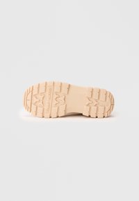 Semelle de chaussure beige avec un motif de profondeur et "Tommy Hilfiger" embossé au centre, présentée sur un fond blanc.