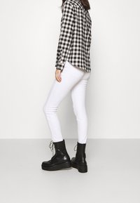 Chemise à carreaux noir et blanc, jean skinny blanc et bottines à plateforme noires à lacets. La chemise a un col pointu et des manches longues.