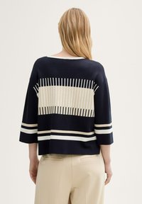 Pull à manches courtes bleu marine avec des rayures horizontales crème et blanches et des lignes verticales au dos, offrant une coupe décontractée et une texture douce.