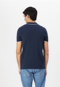 Navy blue polo shirt with a collar and short sleeves, featuring white accents on the edges. Worn with light blue denim jeans.